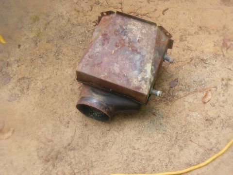1978 Ford Bronco - This rusty metal component with a pipe outlet is shown resting on the ground.