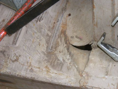 1978 Ford Bronco - This is a close-up view of a damaged and rusted vehicle floor pan, showing a hole and some tools.
