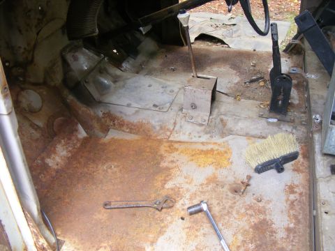 1978 Ford Bronco - The interior floor of a vehicle shows significant rust and is equipped with a floor shifter, a wrench, and a brush.