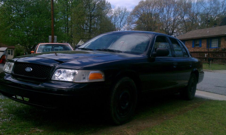 Black 2003 Ford Crown Victoria parked on grass, front 3/4 view, with another vehicle behind it
