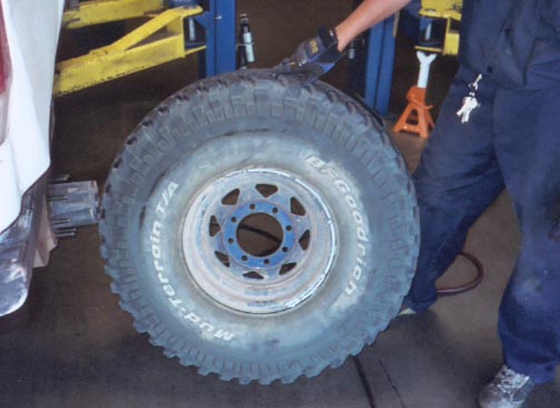 Person holding a BFGoodrich Mud-Terrain T/A tire on a steel 8-lug wheel inside a shop