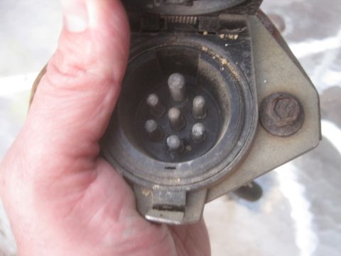 1993 Ford Bronco - A hand holds a trailer hitch connector with six pins, showing wear and dust. The Supermotors.net logo is in the lower right corner.