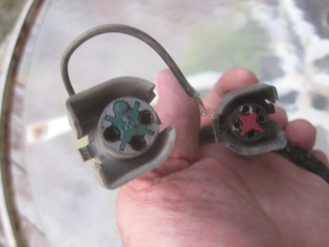 1993 Ford Bronco - Two electrical connectors are held in a hand, one with a green interior and the other with a red interior.