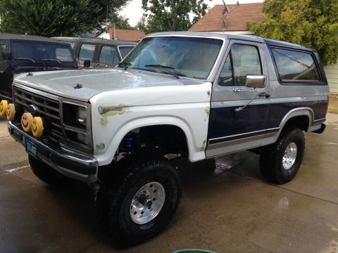 1986 Ford Bronco - A two-tone Ford Bronco with a white fender and yellow fog lights sits in a driveway.