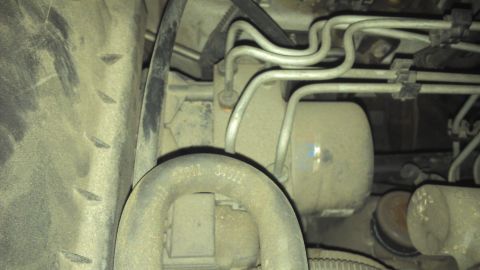 1991 Ford LTD Crown Victoria - Undercarriage view showing various mechanical parts and a portion of a tire. Some text is visible on a pipe.