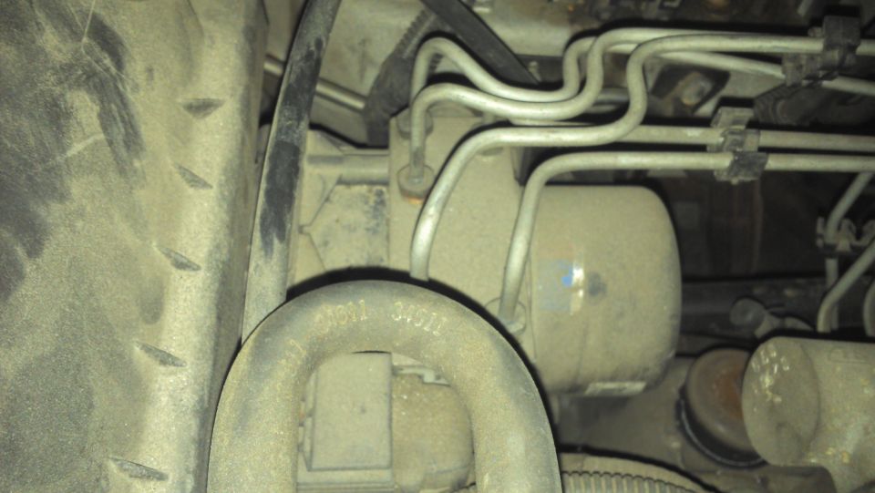 Close-up of vehicle undercarriage with hoses and a tire visible. Text '9N811 34921' is on a metal pipe