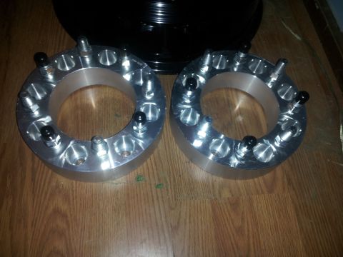 1988 Ford Bronco - Two aluminum wheel spacers are shown on a wooden surface, each with multiple lug studs and black covers.