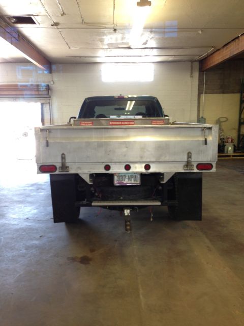 1999 Ford F-250 - The rear of a flatbed truck is shown inside a garage. The truck has a silver bed and dual rear wheels.