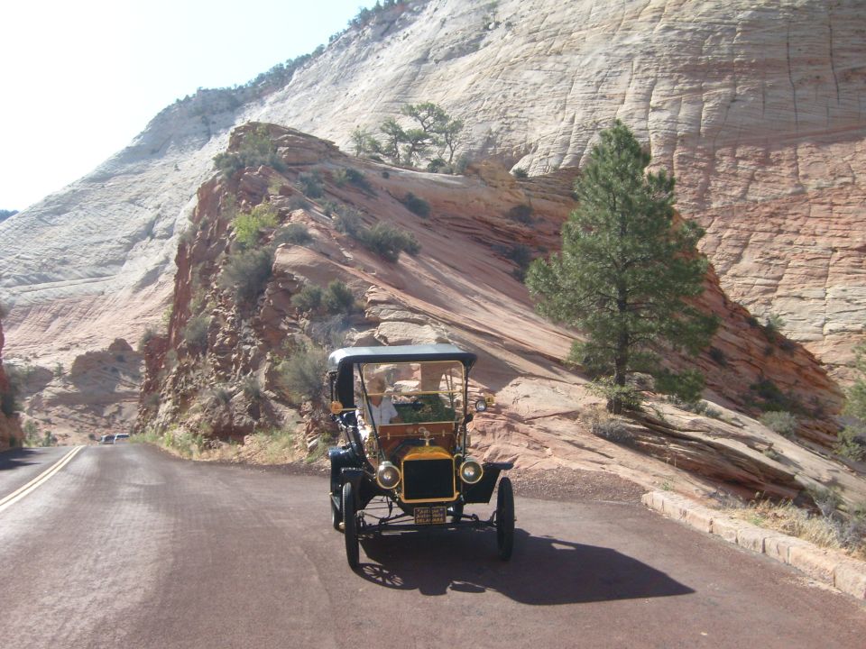Black brass-era touring car driving on a canyon road past red sandstone cliffs