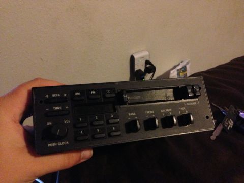 1992 Ford F-150 - A hand holds a black factory AM/FM cassette head unit pulled from a dash, its faceplate showing SEEK, TUNE, six preset buttons, a PUSH CLOC…
