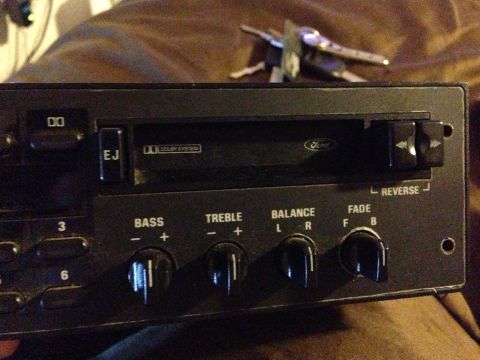 1992 Ford F-150 - Close-up of the right half of a black Ford factory cassette stereo faceplate resting on a couch, showing the Dolby-system tape slot with a…