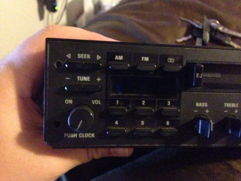 1992 Ford F-150 - A hand holds a black factory-style AM/FM cassette head unit out of the dash, with SEEK and TUNE rocker buttons, six numbered presets, a "PU…