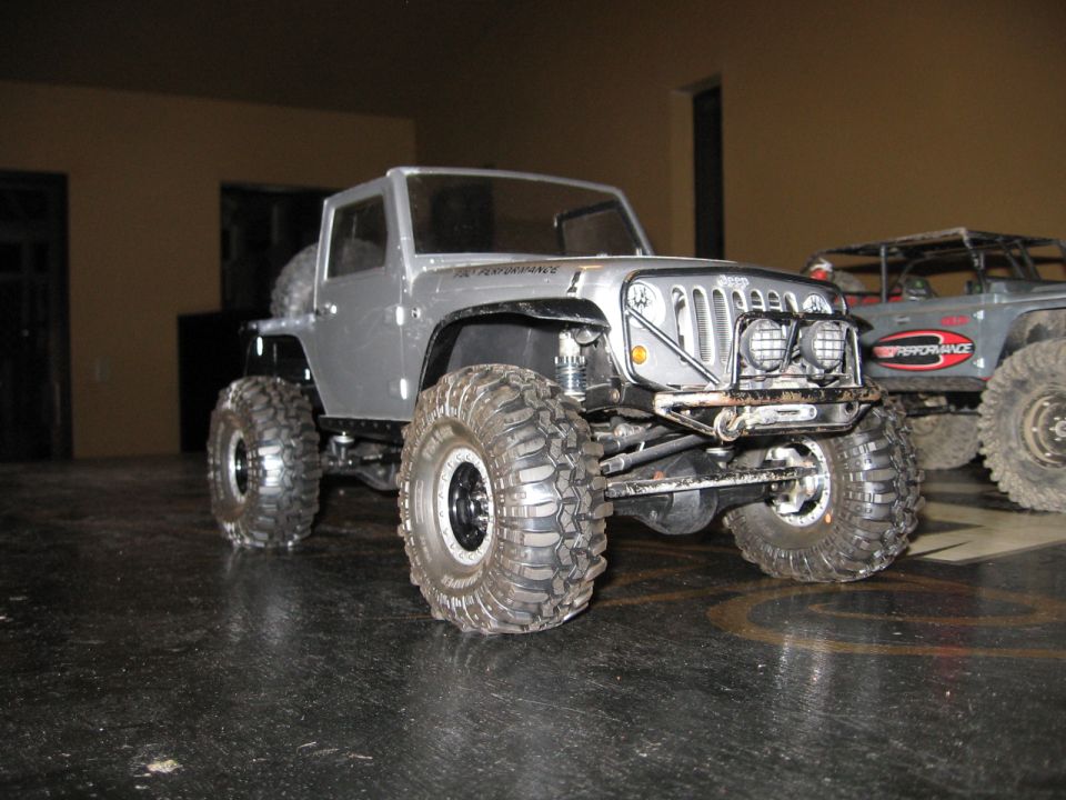 Silver toy RC Jeep Wrangler with large tires and custom bumper, parked indoors
