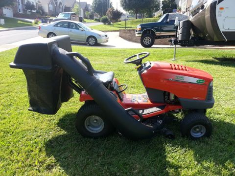1995 Ford Bronco - A red riding mower with a grass bagger is parked on a lawn, with a green Ford Bronco and a silver sedan in the background.