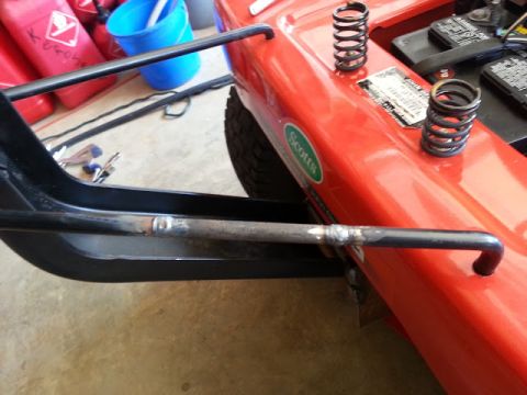 1995 Ford Bronco - Close-up of a red riding mower's deck, showing springs and a battery, with a handlebar attached.