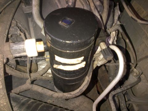 1994 Ford Bronco - Close-up view of a black cylindrical engine component with visible white stripes and a small blue emblem on top.