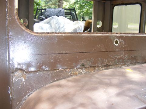 1978 Ford Bronco - A close-up of a heavily rusted metal panel inside a vehicle, with another vehicle partially covered in the background.