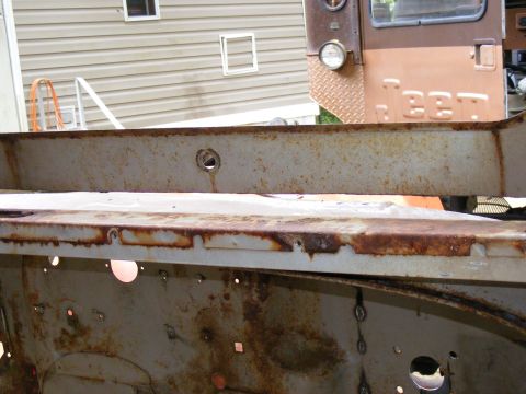 1978 Ford Bronco - Close-up of heavily rusted vehicle frame sections, with a portion of a brown vehicle cab in the background.