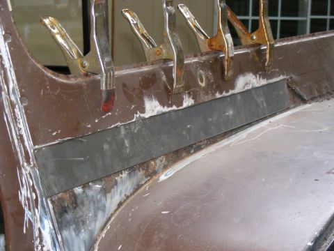1978 Ford Bronco - Close-up of a metal panel undergoing repair with clamps and a new metal insert, revealing rust and preparation for welding.