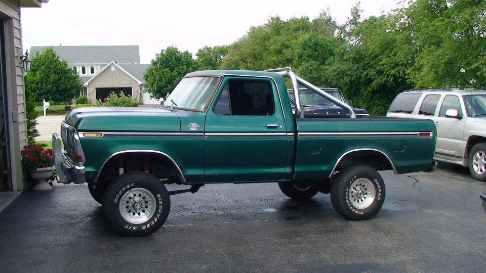 Green pickup truck with roll bar parked next to a silver SUV