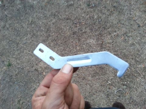 1978 Ford Bronco - A metal bracket, likely a motor rebuild part, is held up for inspection against a dry, grassy surface.