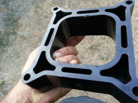 1978 Ford Bronco - A hand holds a black intake manifold part, revealing its internal structure and mounting points.