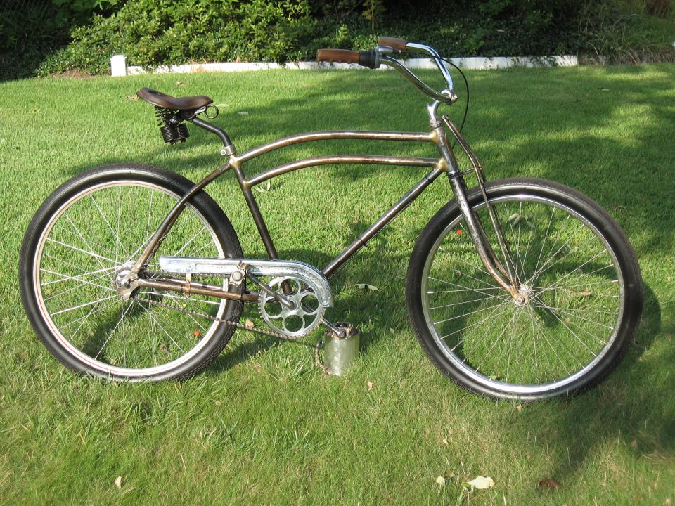 Custom cruiser bicycle with a metallic brown frame, brown grips, and a black seat on a grassy lawn