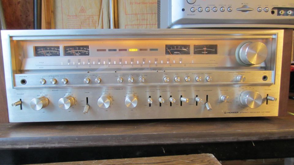 Vintage Pioneer silver stereo receiver with lit dial and VU meters on a wooden shelf