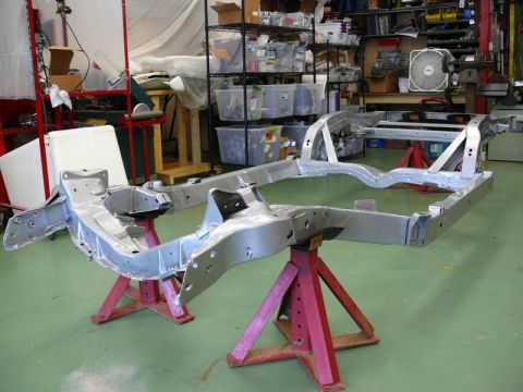 1976 Chevrolet Corvette - The chassis of a vehicle is displayed on red jack stands in a workshop setting, with shelves of parts in the background.