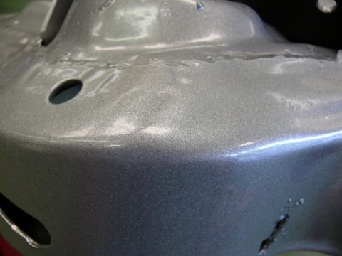 1976 Chevrolet Corvette - Metallic gray painted car part shows welds and circular holes, suggesting it's a component of a vehicle's structure.