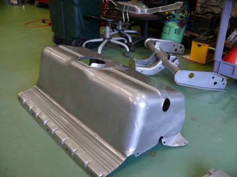 1976 Chevrolet Corvette - Unidentified bare metal car part with a ribbed edge and a circular cutout is shown in a workshop setting.