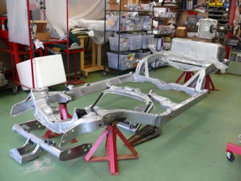 1976 Chevrolet Corvette - The bare frame of a car is supported by red jack stands in a cluttered workshop environment.