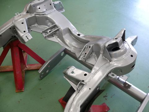 1976 Chevrolet Corvette - Car frame chassis sections are painted silver and supported by red jack stands on a green floor.