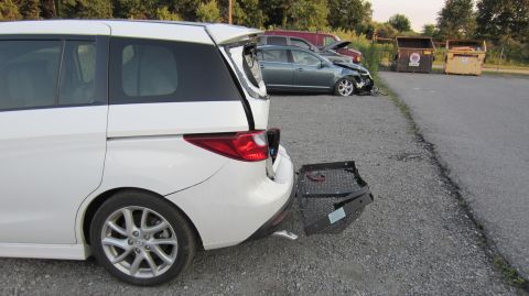 2012 Mazda Mazda 5 - A white 2012 Mazda Mazda 5 is seen from the rear with its hatch damaged and a cargo carrier attached, with other damaged vehicles in the ba…