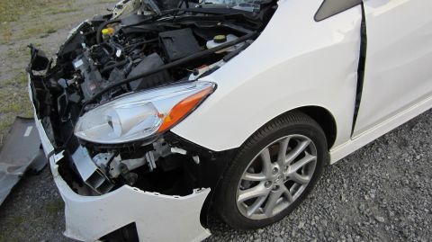 2012 Mazda Mazda 5 - This damaged white Mazda 5 shows significant front-end collision impact, with the engine exposed and the driver's side door deformed.