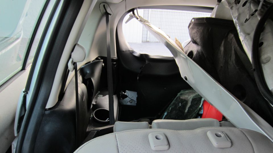 Interior of a white vehicle with damaged rear cargo area, showing torn upholstery and a broken window