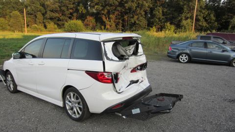 2012 Mazda Mazda 5 - White minivan shows significant rear collision damage, with parts detached and lying on the ground.