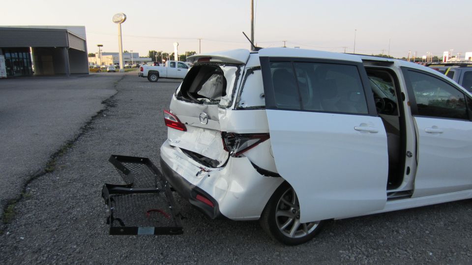 White minivan with rear-end damage, sliding doors open. Trailer hitch attachment on the ground