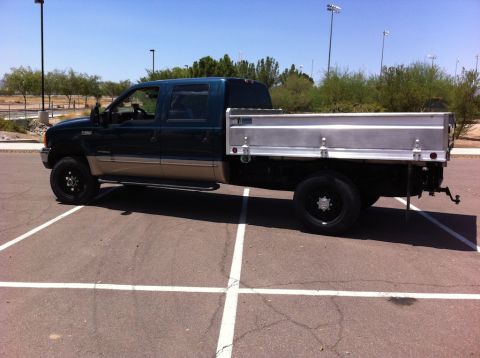 1999 Ford F-250 - A 1999 Ford F-250 pickup truck with a custom flatbed is parked in a lot on a sunny day.