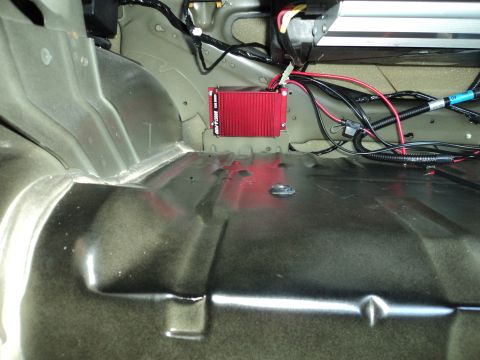 2004 Mercury Grand Marquis - Close-up of a red electronic module and wiring installed in the trunk of a vehicle.