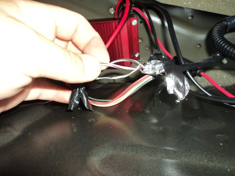 2004 Mercury Grand Marquis - Close-up of a hand connecting wires to a red electronic component, with black tape securing some connections.