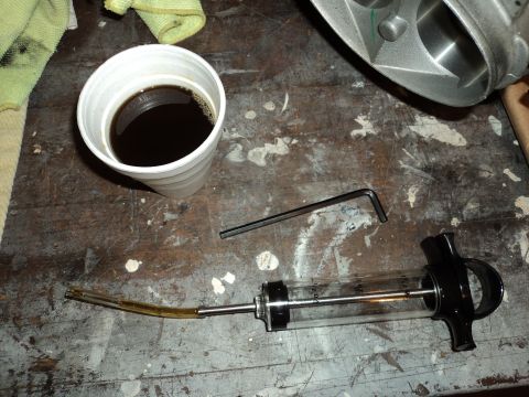 2004 Mercury Grand Marquis - A close-up view shows an engine component, a syringe filled with dark fluid, and an Allen wrench, suggesting automotive maintenance or modi…