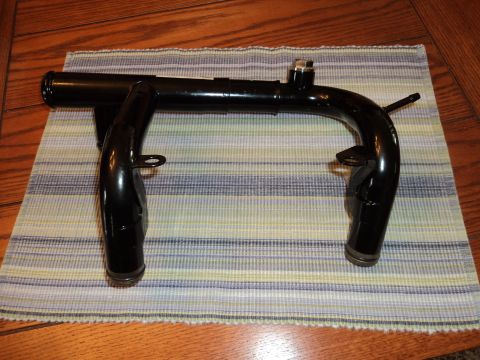 2004 Mercury Grand Marquis - A black metal engine coolant pipe with two outlets and a mounting bracket is shown on a striped cloth.