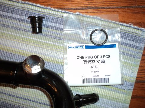 2004 Mercury Grand Marquis - A black automotive pipe and a package of Ford Genuine Parts seals are laid out on a striped cloth.