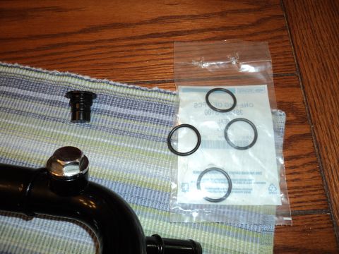 2004 Mercury Grand Marquis - A collection of automotive parts, including a black pipe, a bolt, a cap, and several O-rings, laid out on a striped cloth.