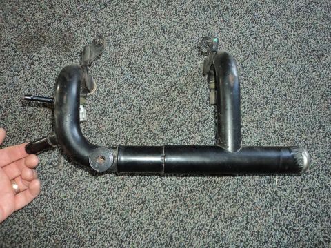 2004 Mercury Grand Marquis - A close-up view of a black metal automotive pipe with connectors and mounting brackets against a carpeted background.