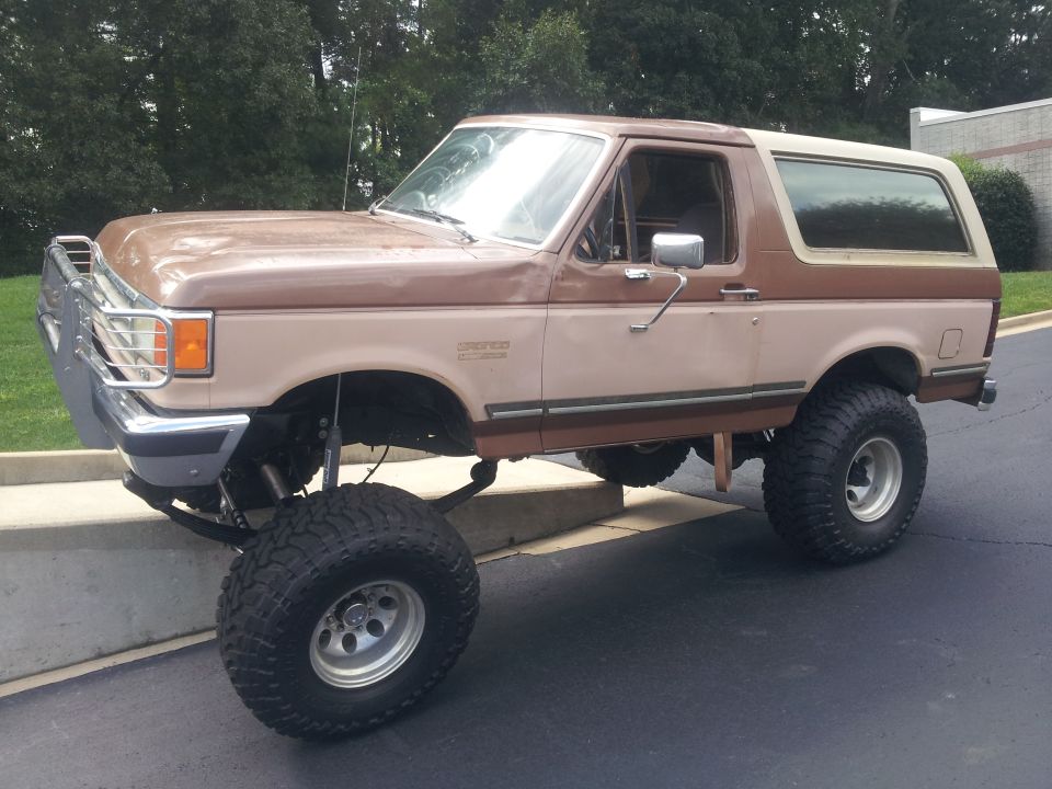 Lifted two-tone brown Ford Bronco with large tires parked on a slight incline