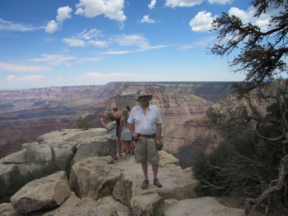 People stand on rocks overlooking the Grand Canyon under a blue sky with clouds