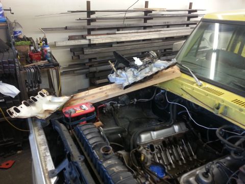 1978 Ford Bronco - The engine bay of a yellow vehicle is shown with engine parts removed and placed on a wooden plank.