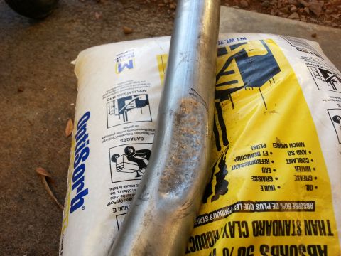 1978 Ford Bronco - An exhaust pipe is shown resting on bags of absorbent material, with visible rust and damage.